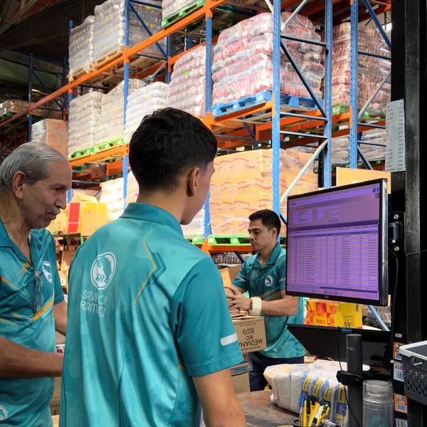 Warehouse workers in teal uniforms checking inventory on a computer screen.
