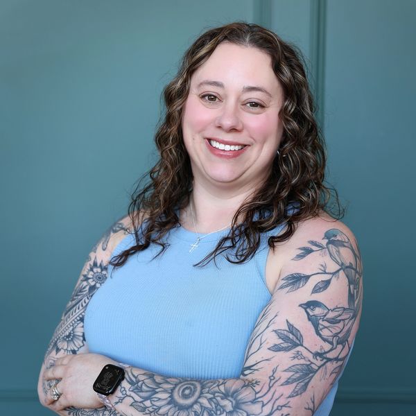 Smiling woman with curly hair and extensive floral and bird tattoos on her arms.
