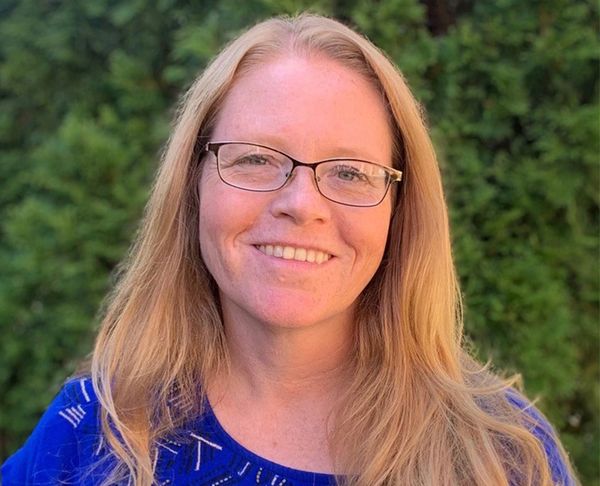 Smiling woman with glasses and long blonde hair outdoors.