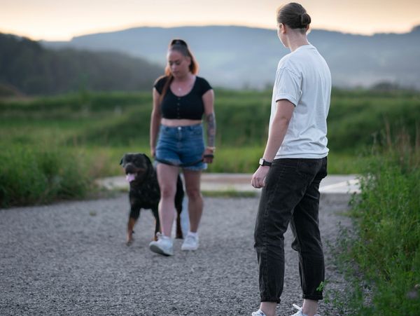 Two people and a dog walking on a gravel path in a natural setting during sunset.
