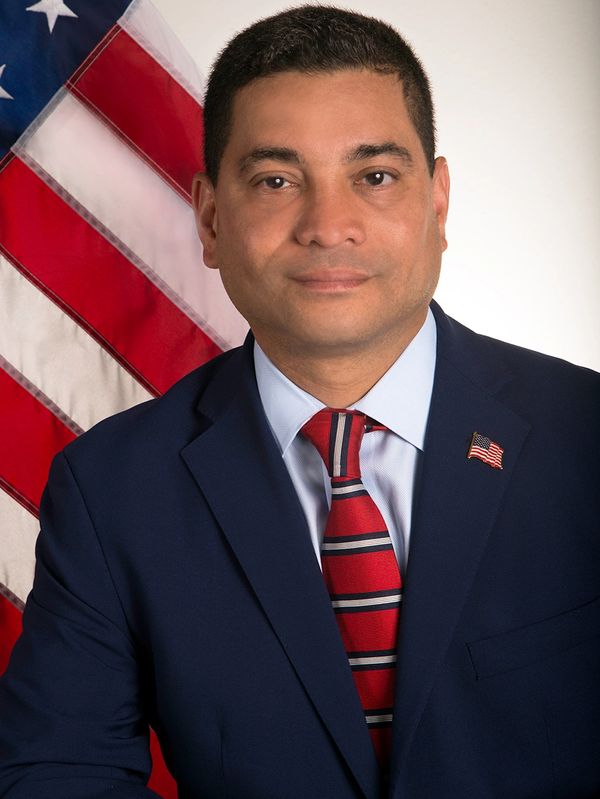 Professional portrait of a man in a suit with an American flag background.