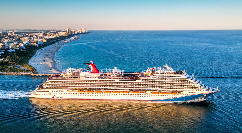 Large Carnival cruise ship sailing near a coastline.