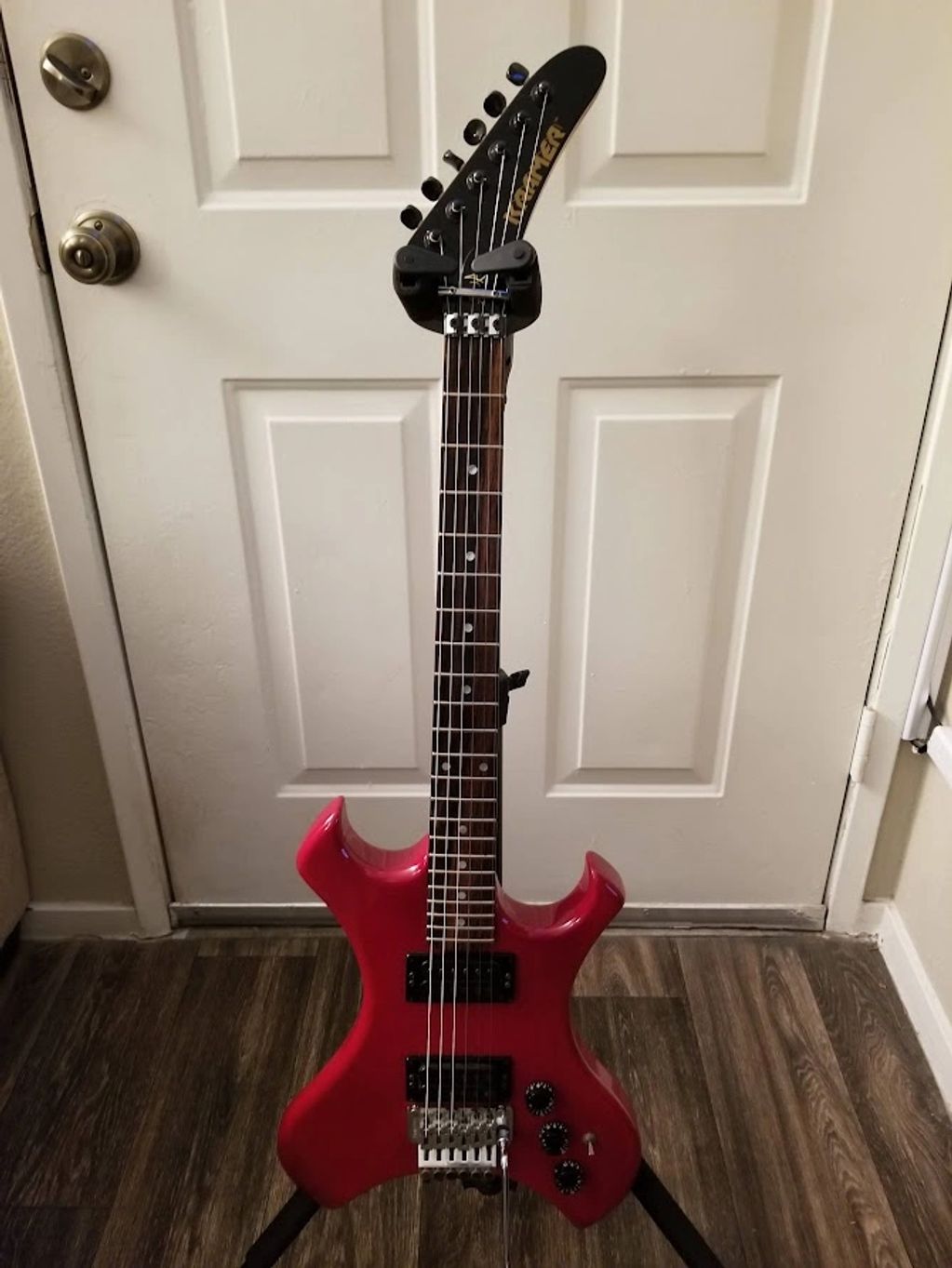 Red electric guitar with unique shape standing on a floor stand.