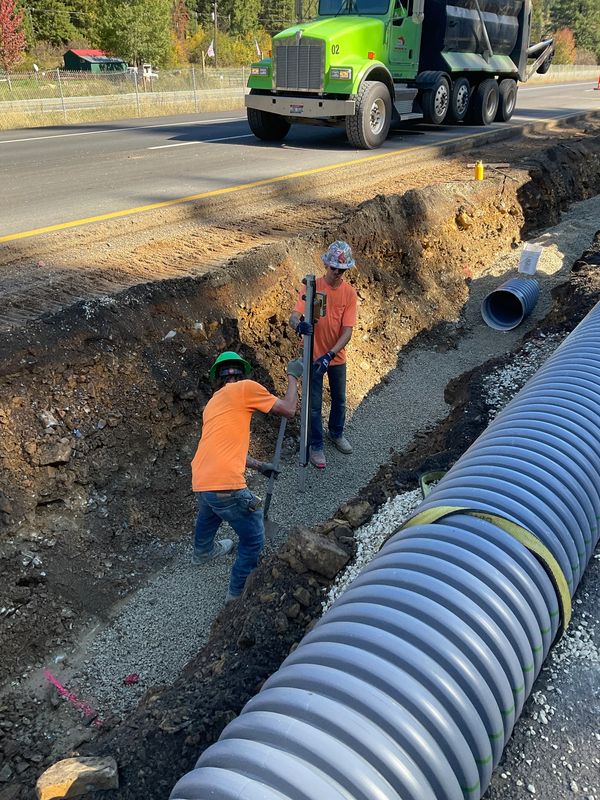 Two construction workers install drainage pipes along a roadside trench.