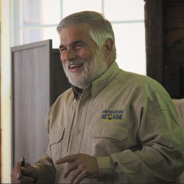 Smiling man in a beige shirt with a Nevada logo.