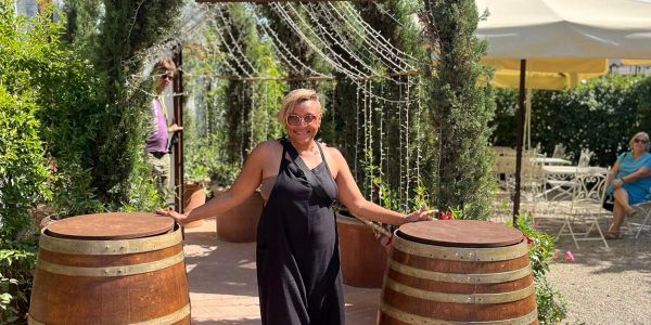 Woman in black dress standing between two wooden barrels outdoors.