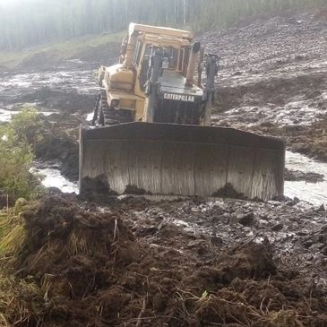 A Caterpillar bulldozer working on muddy terrain in a forested area.