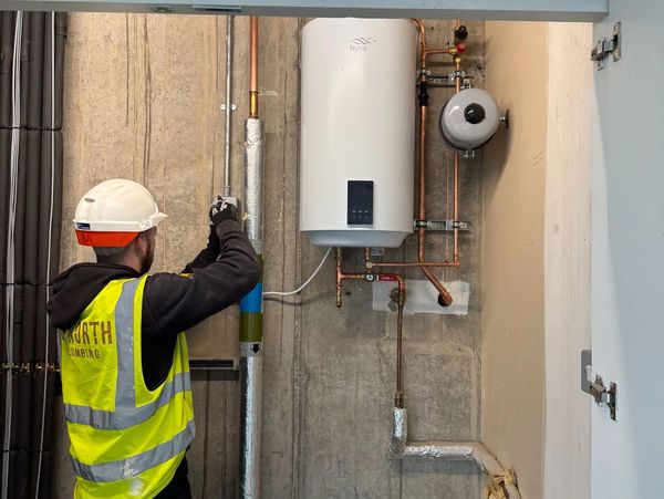 Worker in safety gear inspects pipes and water heater.