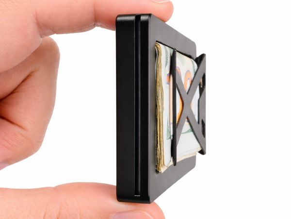 Hand holding a slim black money clip with folded cash inside.