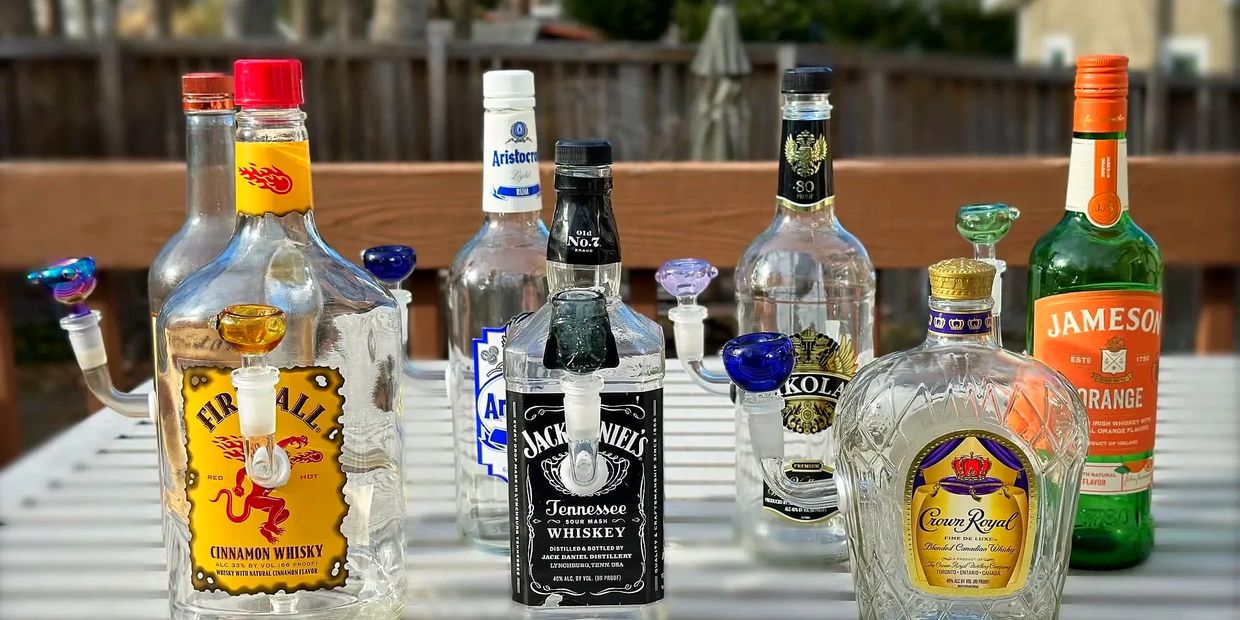 Empty whiskey bottles converted into glass water pipes arranged on a table outdoors.