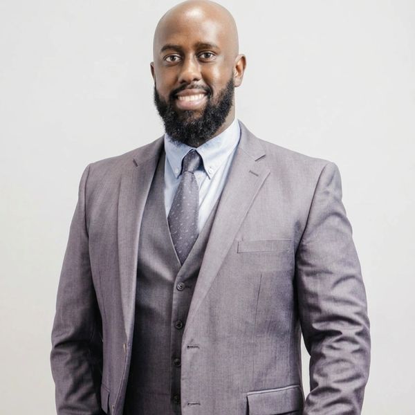 Smiling man in a grey suit and tie against a plain background.