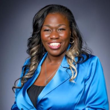 Confident woman smiling in a blue blazer against a gray backdrop.