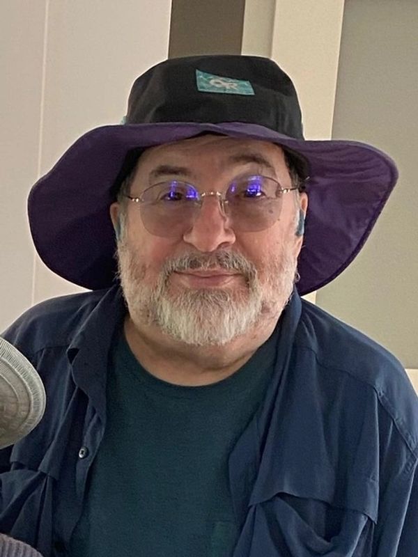 Smiling man with a beard wearing glasses and a wide-brimmed hat.
