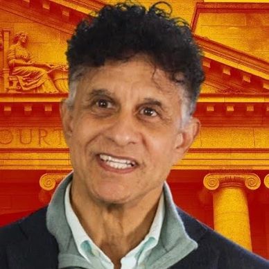 Smiling man with curly hair in front of an orange classical building backdrop.