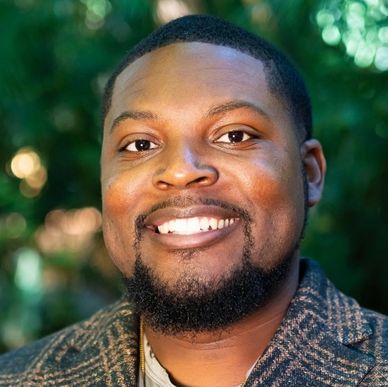 Smiling man with a trimmed beard outdoors in natural light.