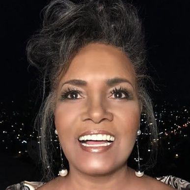 Smiling woman with pearl earrings against a nighttime city backdrop.