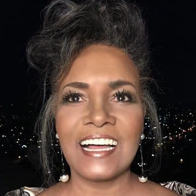 Smiling woman with pearl earrings against a night city backdrop.