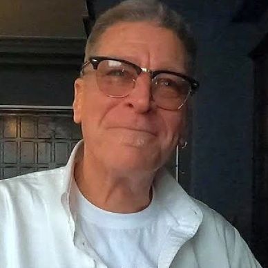 Smiling elderly man wearing glasses and white shirt indoors.