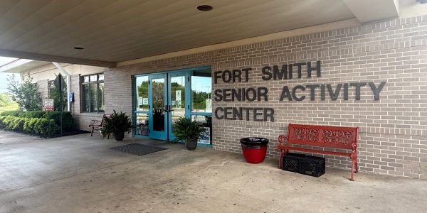 Entrance of Fort Smith Senior Activity Center with a red bench and potted plants.