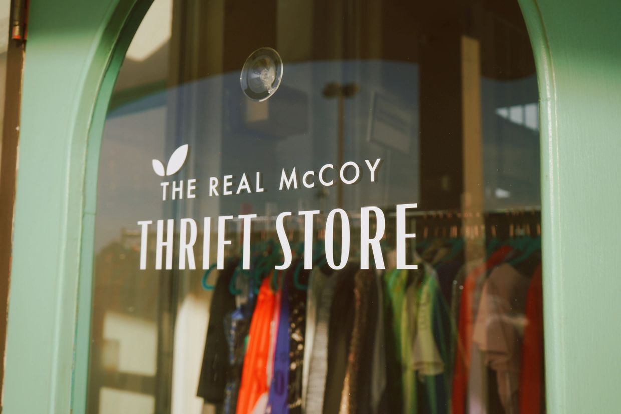 Window sign for The Real McCoy Thrift Store with clothes inside.