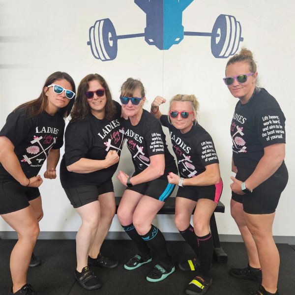 Five women in matching gym outfits flexing muscles indoors.