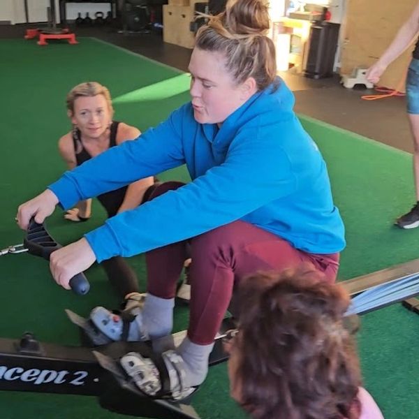 Woman in blue hoodie rowing indoors.