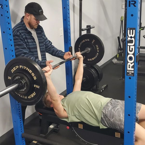 Man bench presses weights with a spotter's help.