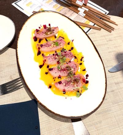 Plate of artfully arranged sashimi with sauce and microgreens.