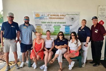 Group of eight people posing together at a golf tournament event.