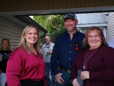 Three adults smiling and posing together at an outdoor gathering.