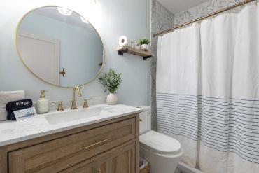 Modern bathroom with round mirror and striped shower curtain.