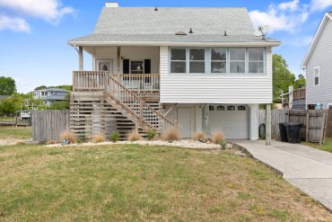 Raised white house with a wooden staircase and garage.