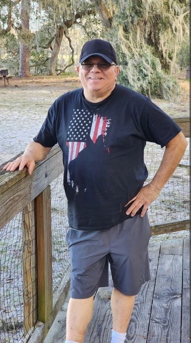 Smiling man in black cap and patriotic shirt outdoors.