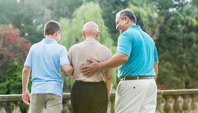 Three generations of men walking together outdoors, supporting each other.