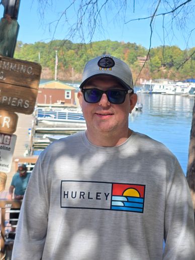 Man wearing sunglasses and a Hurley sweatshirt by the water.