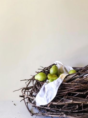 Green pears in a rustic twig nest with white cloth.