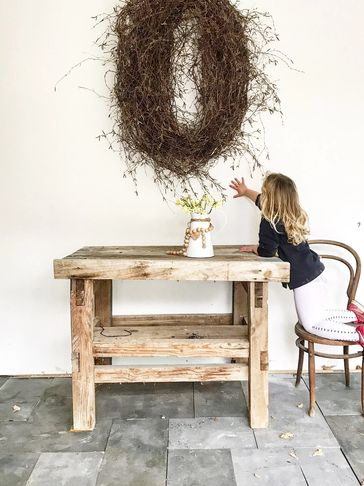 Child reaching up while standing on a chair next to a wooden table.