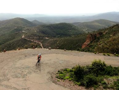 Cyclist on a winding mountain road overlooking green hills.