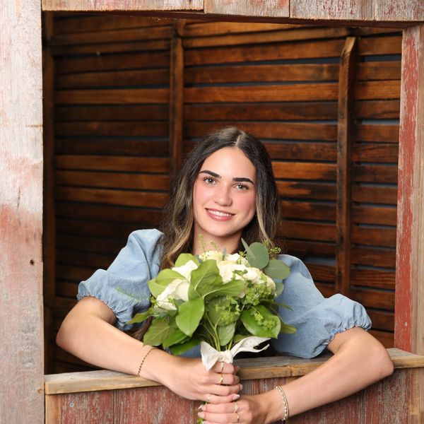 Smiling woman holding a bouquet of flowers by a wooden window frame.