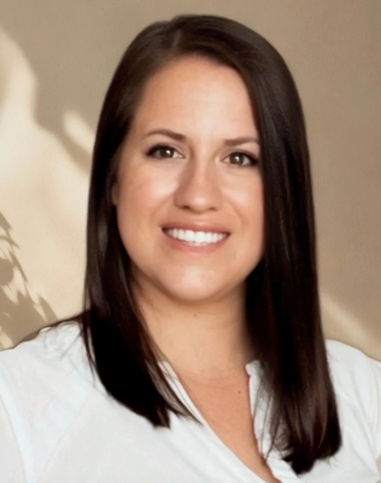 Smiling woman with straight dark hair and a white shirt against a beige background.