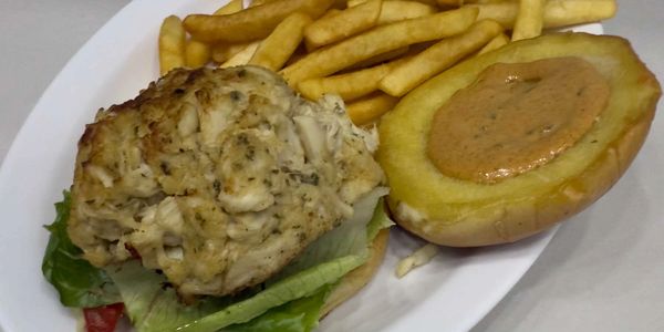 Grilled chicken sandwich with lettuce, tomato, special sauce, and fries on a white plate.