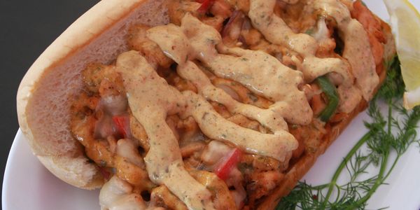 Spicy shrimp po' boy sandwich with creamy sauce on a white plate.