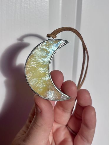Hand holding a crescent moon-shaped pendant with iridescent surface.