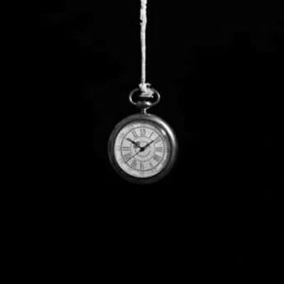 A pocket watch hanging by a string against a black background.