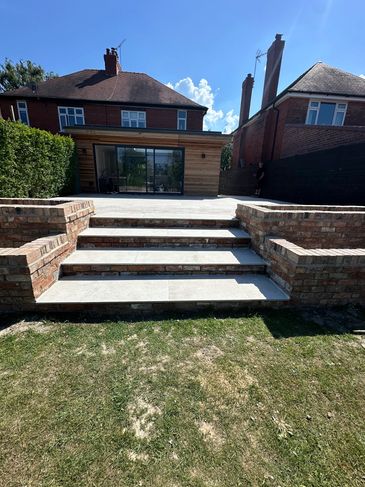 Raised porcelain patio with steps and reclaimed brick planters. 
