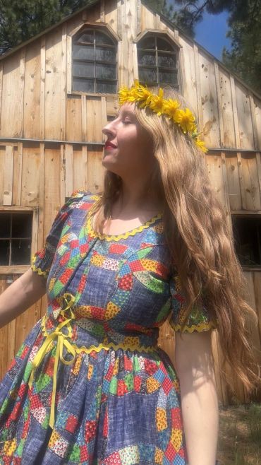 Woman in colorful dress and flower crown outside wooden house.