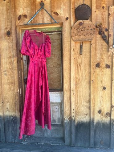 Red dress hanging in a rustic wooden doorway.