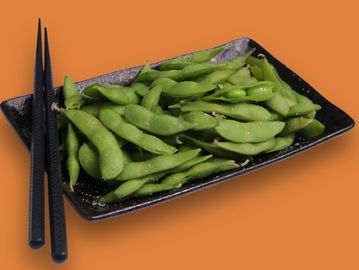 Green edamame pods on a black plate with chopsticks.