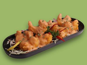 Fried shrimp covered in orange sauce on a black plate.
