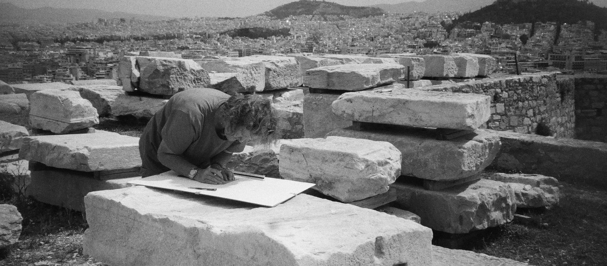 Person sketching on a board among ancient stone ruins in a cityscape setting.